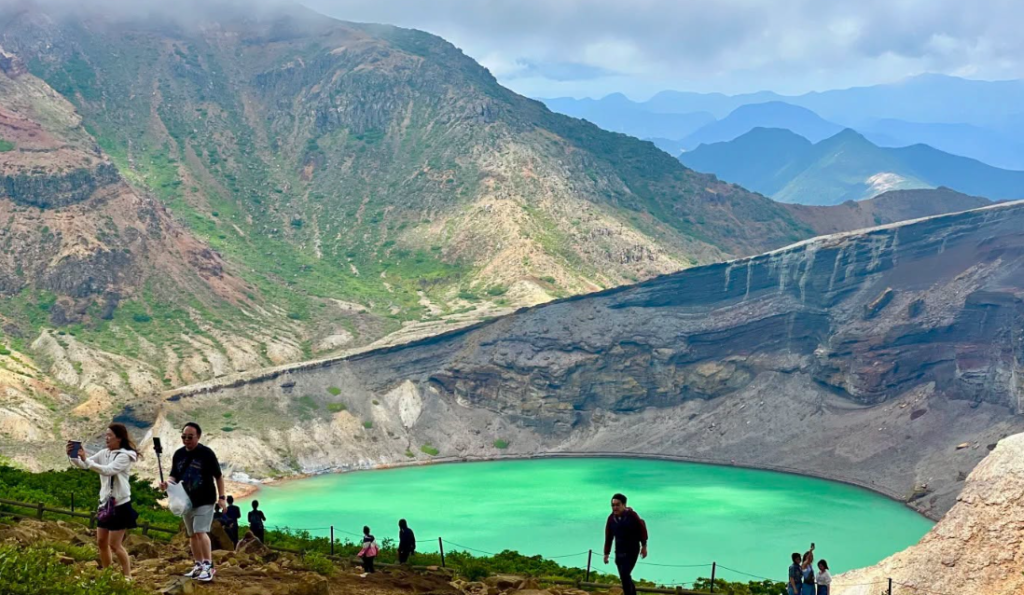 Turquoise waters of the Okama crater lake with visitors on the rim path