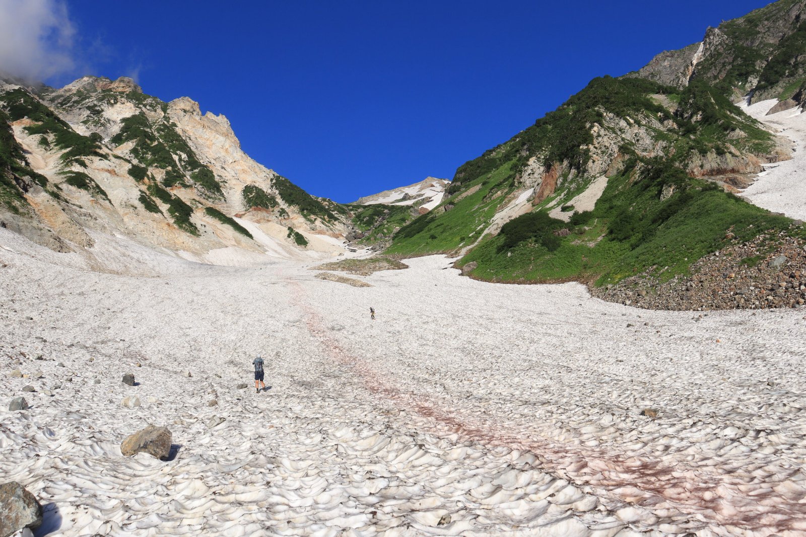 Hikers crossing the Daisekkei snow valley below Mount Shirouma in summer